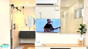 A modern bathroom with a mounted TV, a fan, and a potted plant.