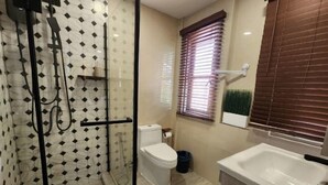 A bathroom with a glass-enclosed shower, a toilet, a sink, and a window with blinds.