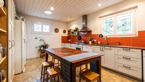 Cozinha com mesa de madeira, banquetas, fogão e geladeira.