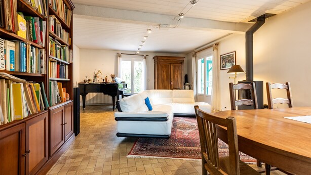Uma sala de estar espaçosa com um sofá branco, uma mesa de jantar de madeira, uma estante de livros e um piano.