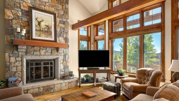 A cozy living room with a stone fireplace, large windows, and comfortable seating.