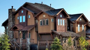 A multi-story log cabin with a stone chimney, wooden balconies, and a stone foundation.