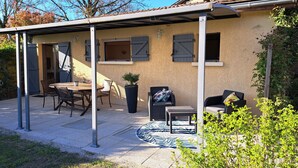 Un patio couvert avec une table et des chaises, une plante en pot et une petite table ronde avec un siège.