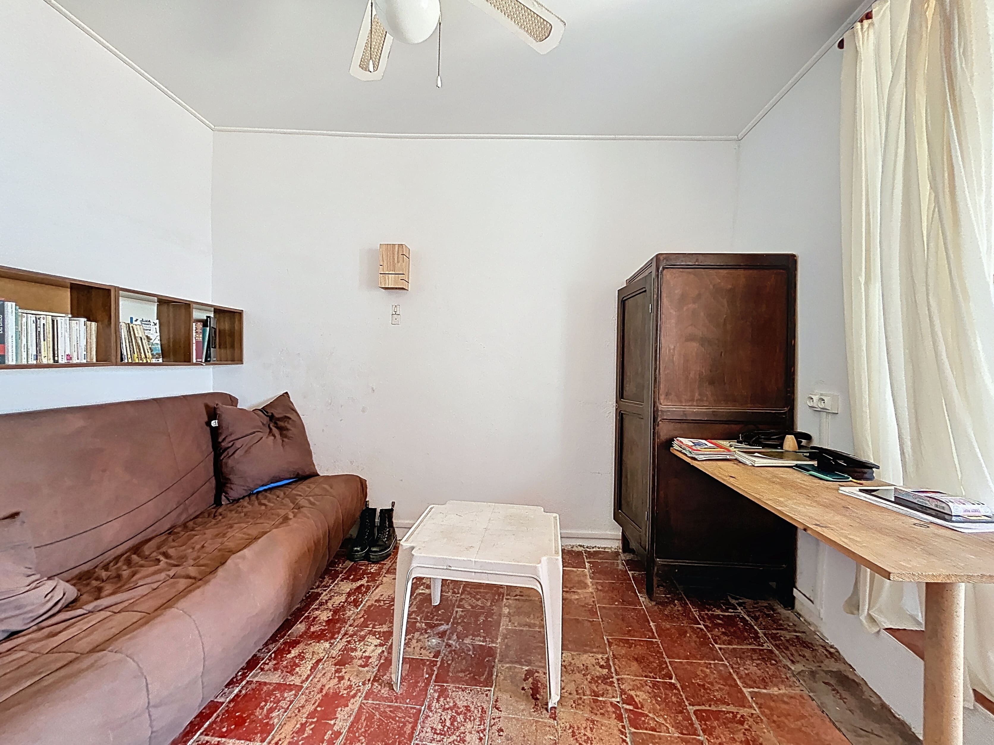A compact living space with a brown sofa, a small white table, a wooden cabinet, and a ceiling fan.