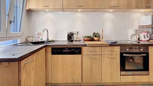 A modern kitchen with wooden cabinets, a dishwasher, an oven, and various appliances including a coffee maker and a kettle. - Charming house with terrace and breathtaking views (Bages)