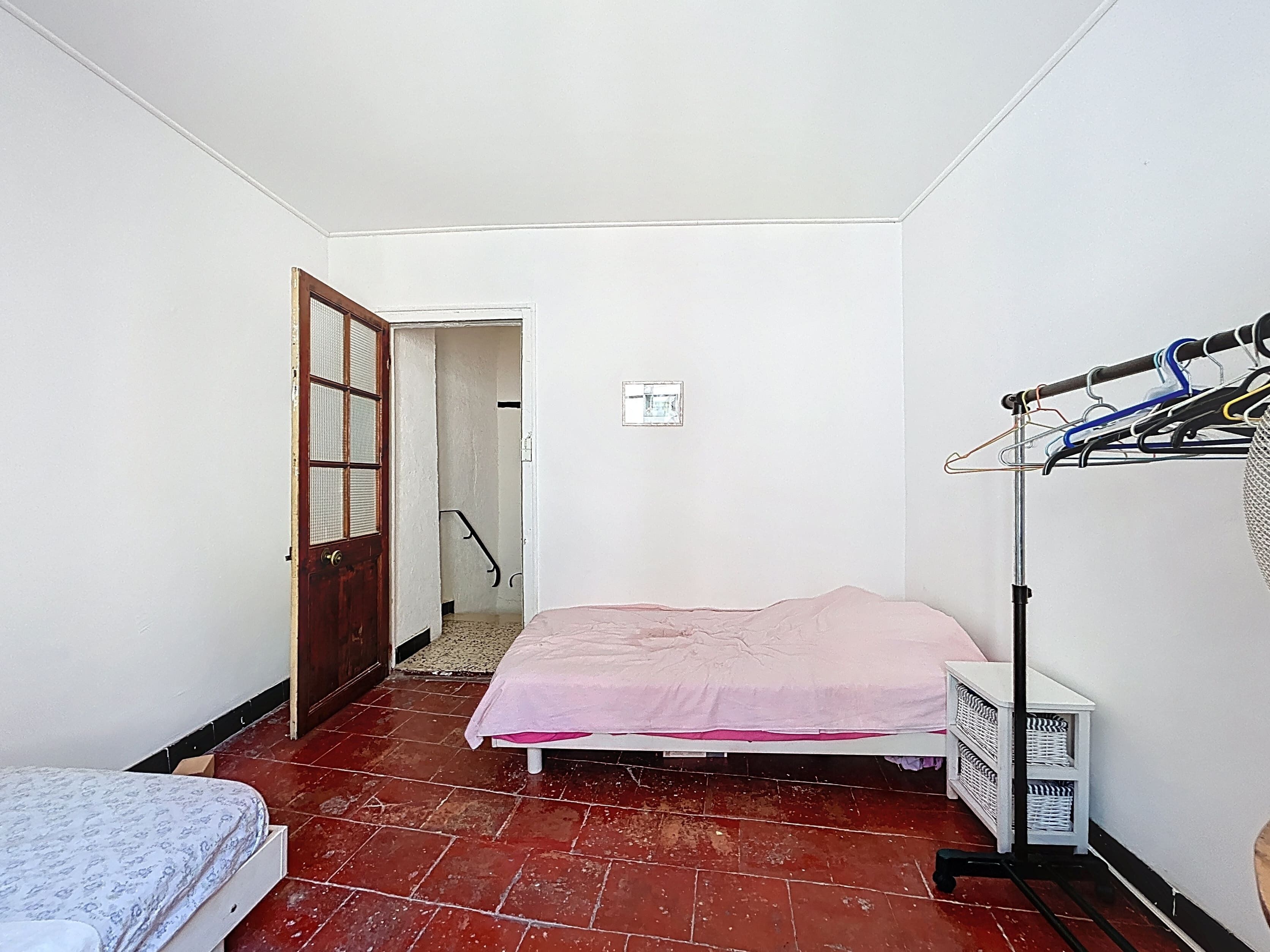 Una habitación pequeña y estrecha con una cama, un armario y una puerta que da a otra habitación.