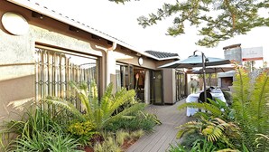 A patio area with a table set for dining, surrounded by lush greenery and a building with a modern design. - Kgarebana Boutique Guesthouse (Sesakhile)