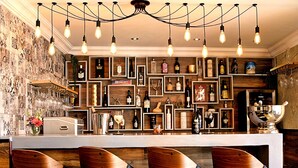 A bar area with wooden shelves, multiple bottles, glasses, and a modern light fixture. - Kgarebana Boutique Guesthouse (Sesakhile)
