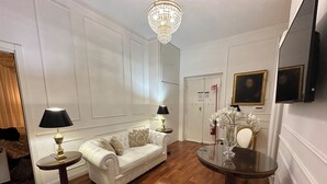 A well-furnished living room with a white sofa, two side tables with lamps, a round glass table, and a chandelier. - Alloggio Turistico King Plaza (Rome)