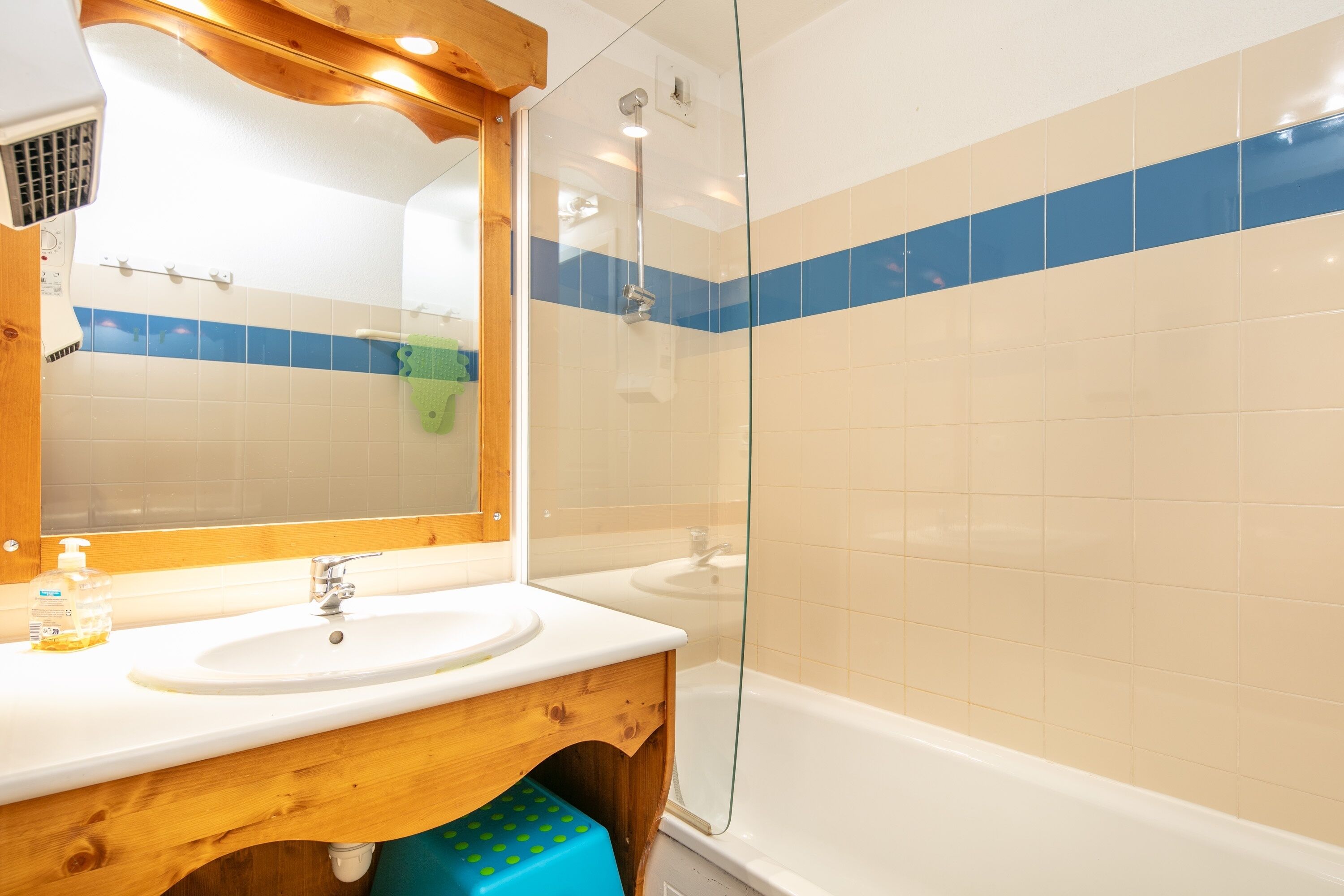 Une salle de bain avec un meuble-lavabo en bois, un évier, un miroir et une douche séparée par une paroi de verre.