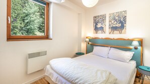 A bedroom with a large window, a bed with white bedding, a headboard with a lamp, and two wall-mounted deer paintings. - OBIOU - 200m des Pistes de Ski (Chamrousse)
