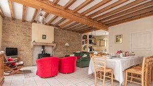 A spacious living area with a fireplace, red sofas, a dining table set for four, and a television in the corner.