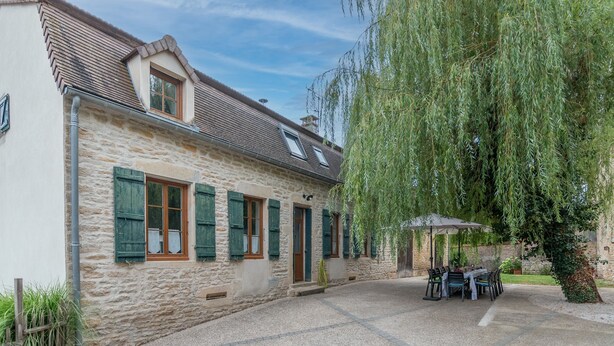 A stone building with a patio area, outdoor seating, and a weeping willow tree.