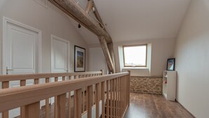 A spacious room with a wooden staircase, white doors, a stone wall, and a window providing natural light.