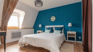A bedroom with a large bed, two bedside tables, a window, and a blue accent wall.