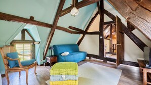 A room with exposed wooden beams, a blue sofa, a wooden chair, and a green and yellow cushion.