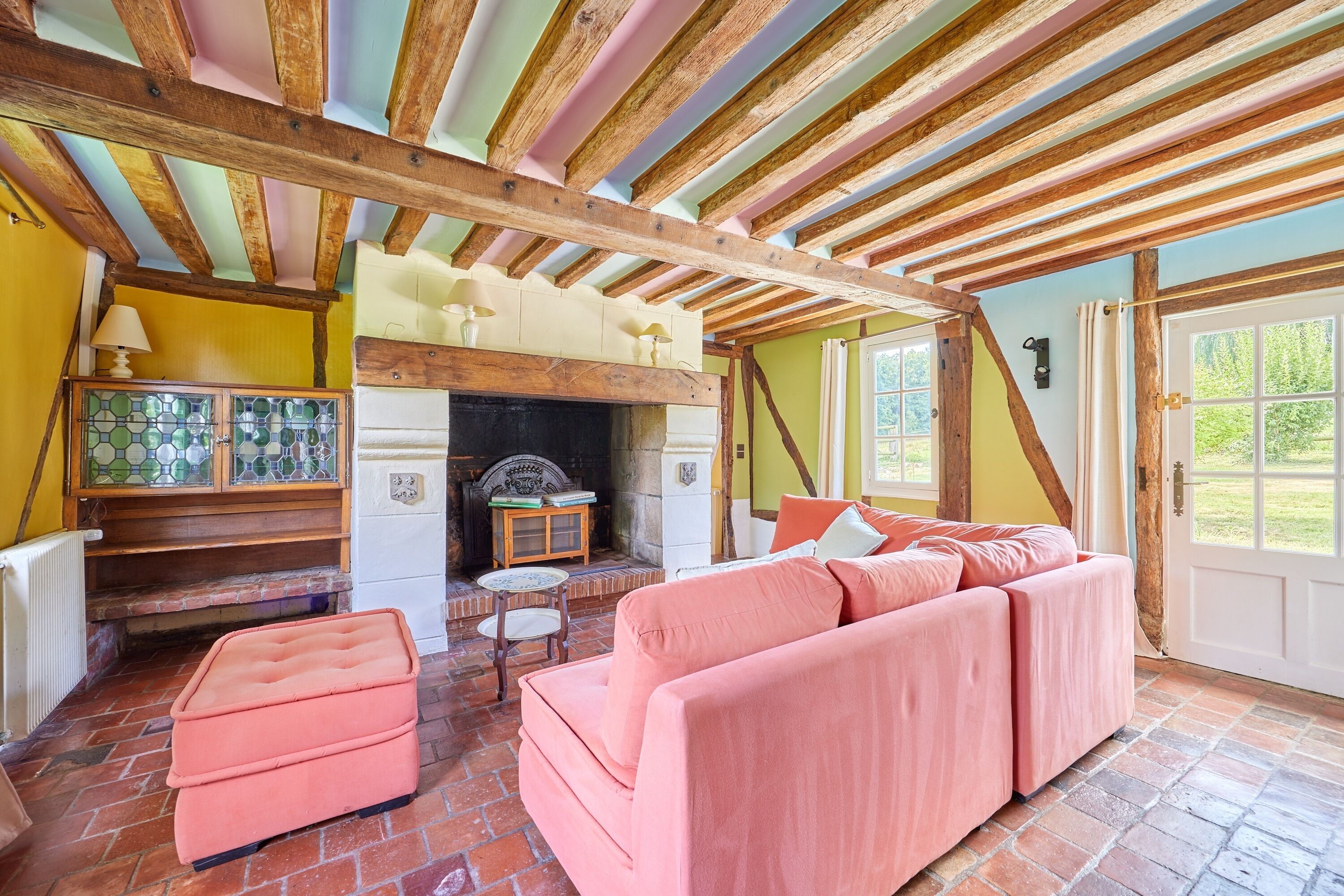 Una habitación acogedora con techo de madera, chimenea, sofá rosa y una mesita con lámpara.