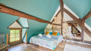 A bedroom with a sloped ceiling, a bed with a floral bedspread, and a stone wall.