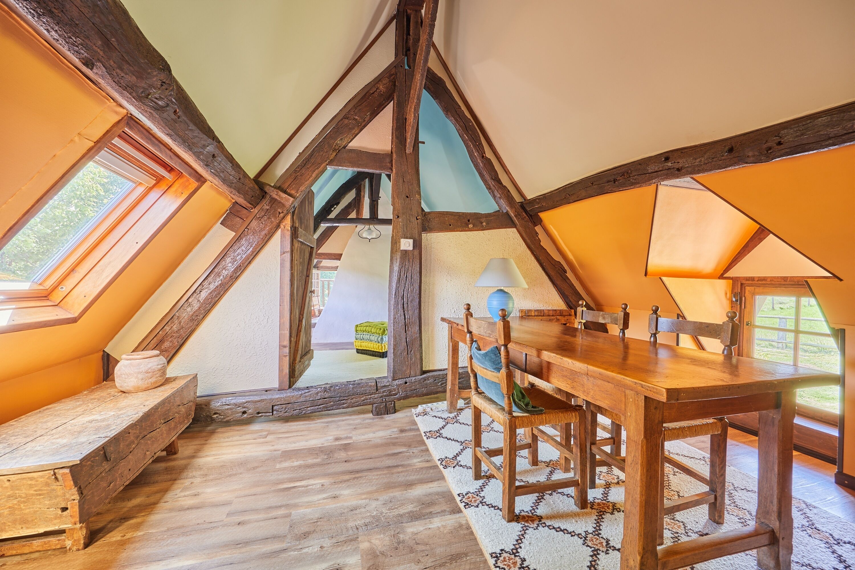Um quarto de sótão acolhedor com uma mesa de madeira e um banco, janelas amplas e teto inclinado.