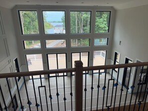 A room with large windows, a wooden railing, and a view of a deck and outdoor area.