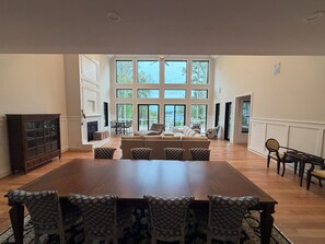 A spacious living room with a large dining table, patterned chairs, a fireplace, and large windows offering a view of the outdoors. - LICENSE TO CHILL II Spacious 8-bedroom Lake Anna house. (Bumpass)