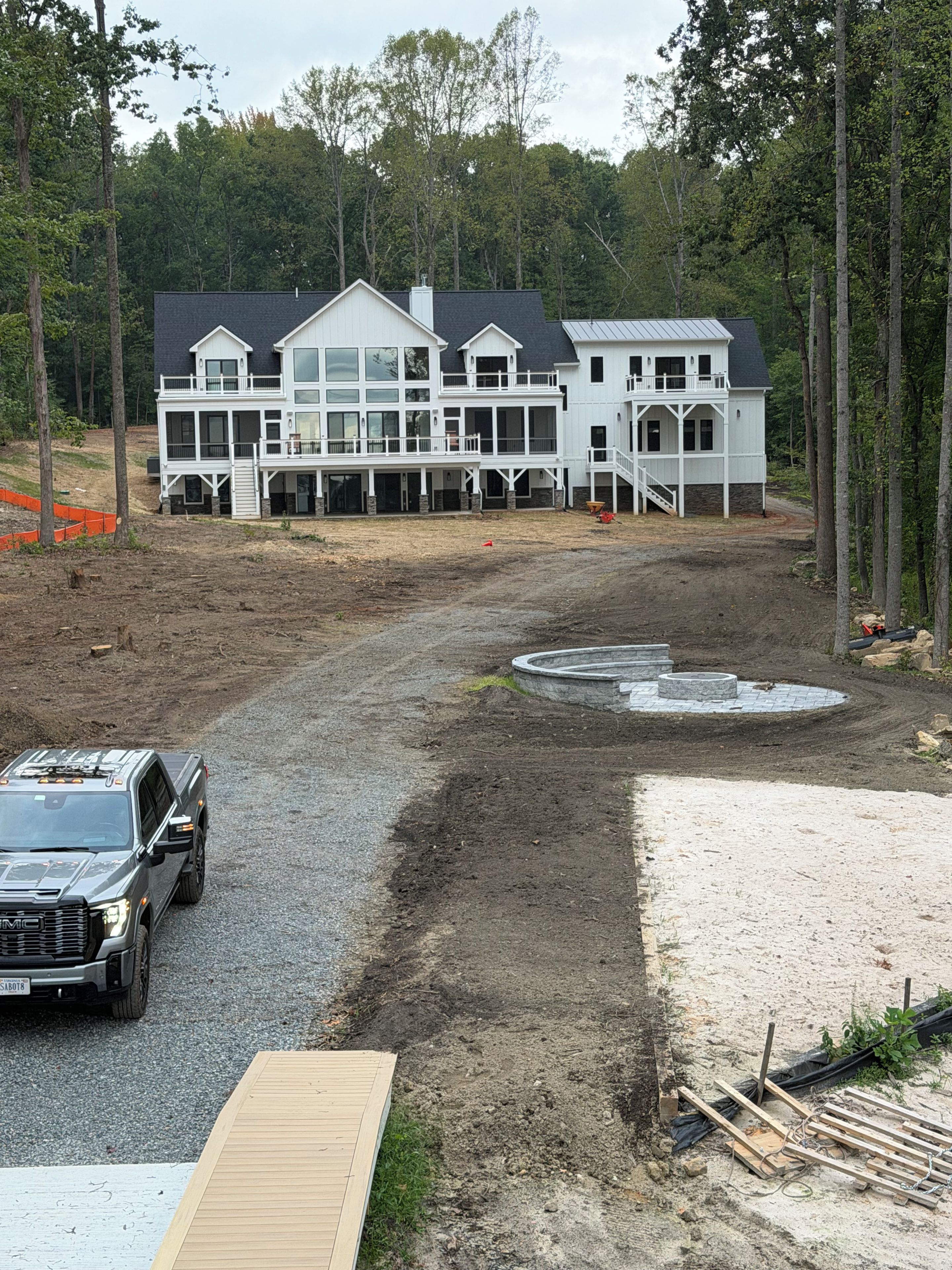 A large, multi-story building with a covered porch area, surrounded by trees and a dirt path.