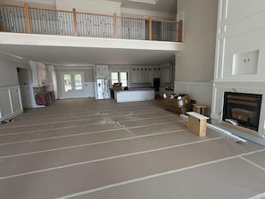A spacious living area with a high ceiling, a kitchen with white cabinets, and a fireplace.
