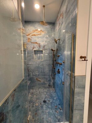 Une salle de bain moderne avec une douche à parois de verre, des murs en marbre et un sol carrelé avec des motifs hexagonaux.