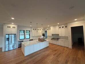 Una cocina moderna con armarios blancos, un refrigerador de acero inoxidable, una isla grande e iluminación colgante.