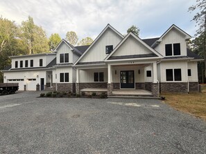 Une maison à deux étages avec un porche à l’avant, des fondations en pierre et une allée.