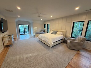 Un dormitorio con una cama grande, una silla, un televisor y un ventanal corredera que da a un balcón.
