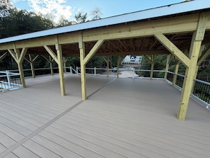 A wooden deck with railings, a covered area, and a view of a building in the background.