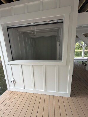 A white outdoor structure with a sliding door, a small window, and a power outlet. - LICENSE TO CHILL II Spacious 8-bedroom Lake Anna house. (Bumpass)