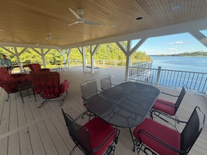 Une terrasse extérieure couverte, dotée d’une table et de chaises, qui offre une vue sur une étendue d’eau.