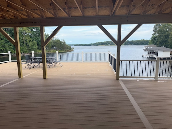 A wooden deck with a view of a lake, a white railing, and a small dock.