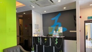 A reception area with a modern design, featuring a black reception desk, a green accent wall, and a large blue logo on the wall. - Lodge 5 (Kota Kinabalu)