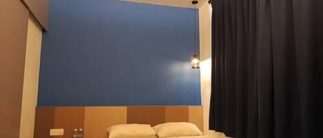 Ein Hotelzimmer mit Bett, Nachttisch, Wandlampe und einem Fenster mit Vorhängen.
