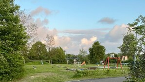 A park with a paved path, a brick wall, and playground equipment. - Cozy detached vacation home with garden around: de Frije Fûgel, Lauwersoog (Lauwersoog)