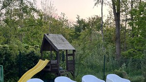 A wooden playhouse with a yellow slide, surrounded by white plastic chairs. - Cozy detached vacation home with garden around: de Frije Fûgel, Lauwersoog (Lauwersoog)