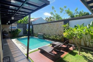 Una piscina con sillones de descanso, un porche cubierto y un muro de piedra.