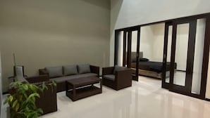 Un salon moderne comprenant un ensemble de canapés, une table basse et une grande porte-fenêtre coulissante donnant sur une chambre.