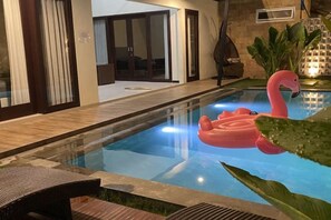 Una piscina con un flotador con forma de flamenco rosa, rodeada por un patio con sillas y una planta.