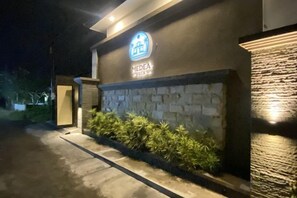 Entrada de un hotel con fachada de piedra, un letrero de neón y un camino bien iluminado.