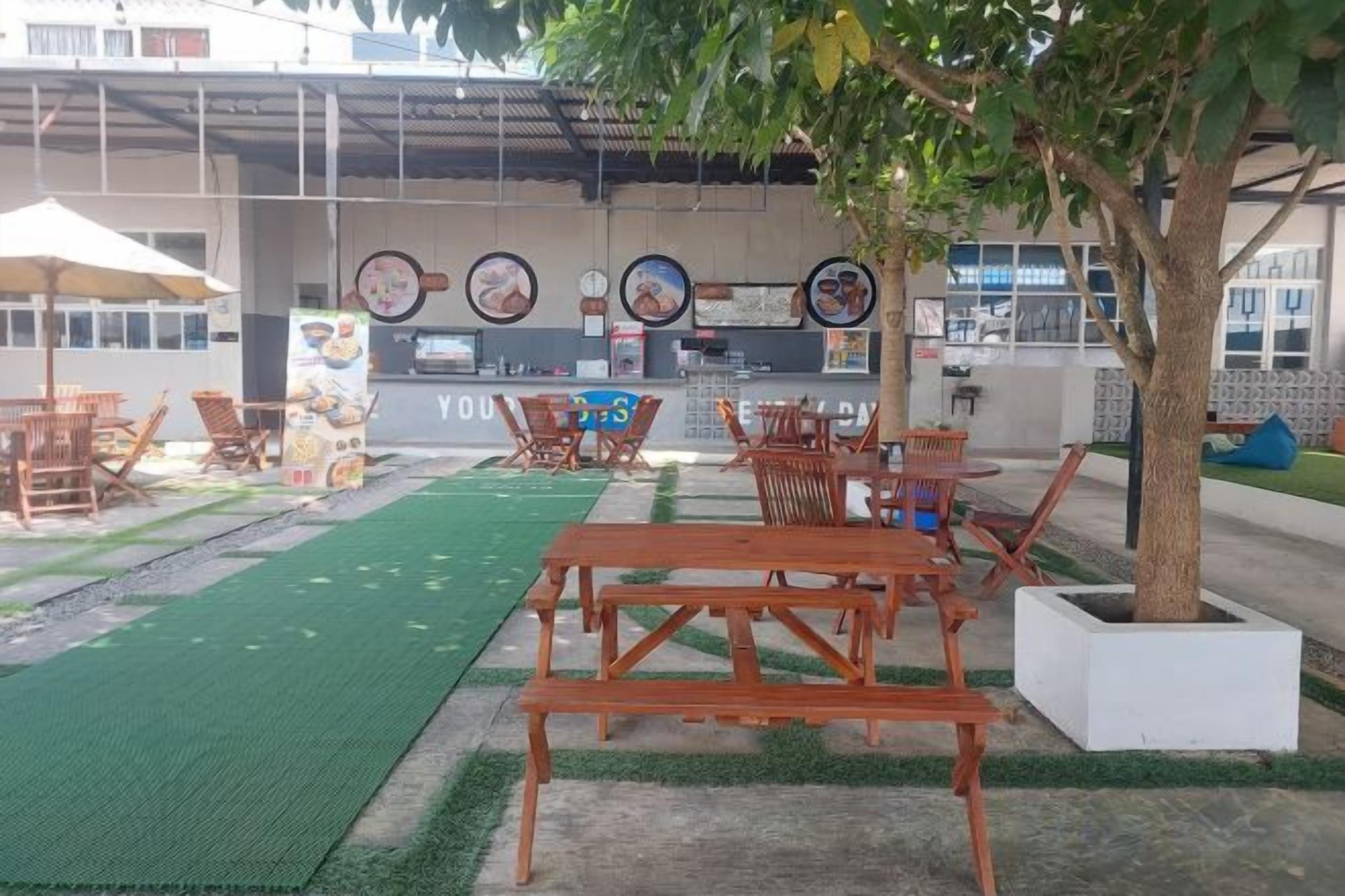 An outdoor seating area with wooden tables and chairs, a green turf, and a building with a sign in the background.