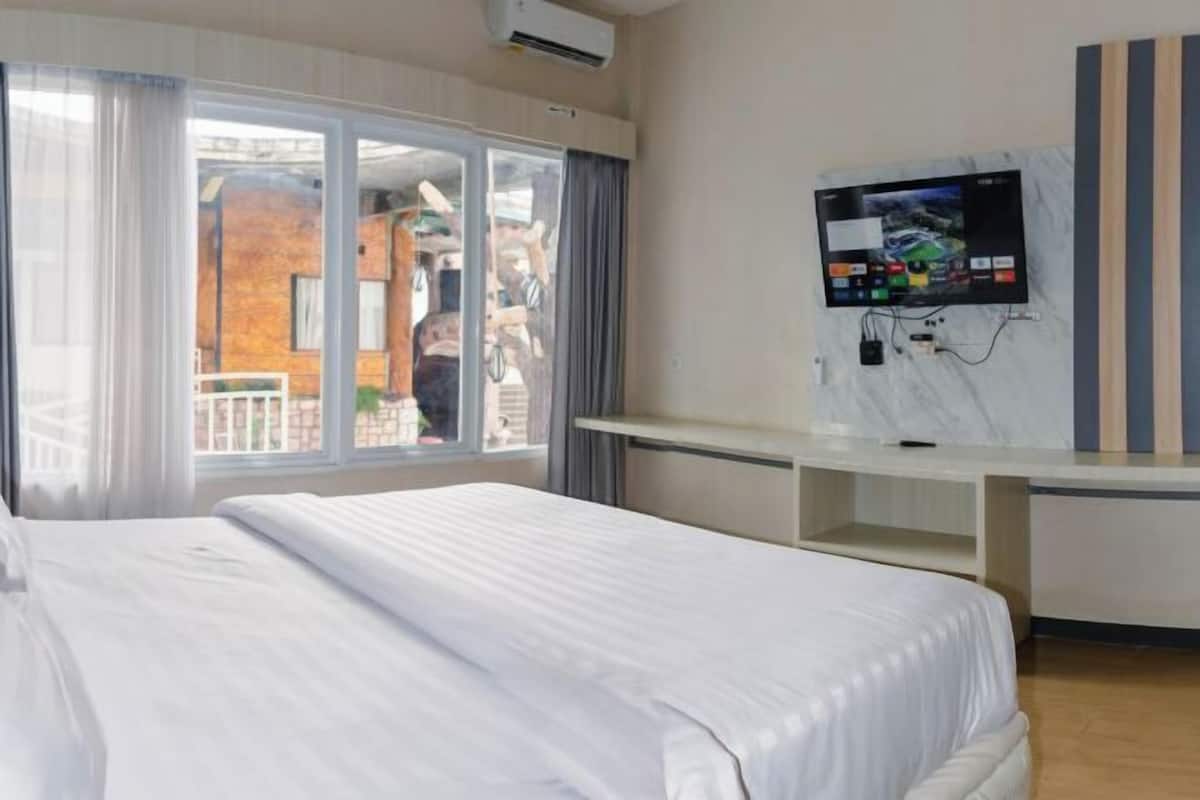Habitación de hotel con cama, televisor montado en la pared, escritorio y vistas a través de un ventanal grande.