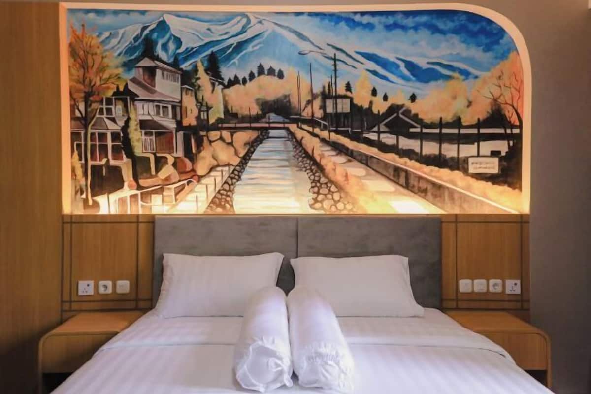 Una cama con ropa de cama y almohadas blancas, un cuadro encima y un cabecero de madera.