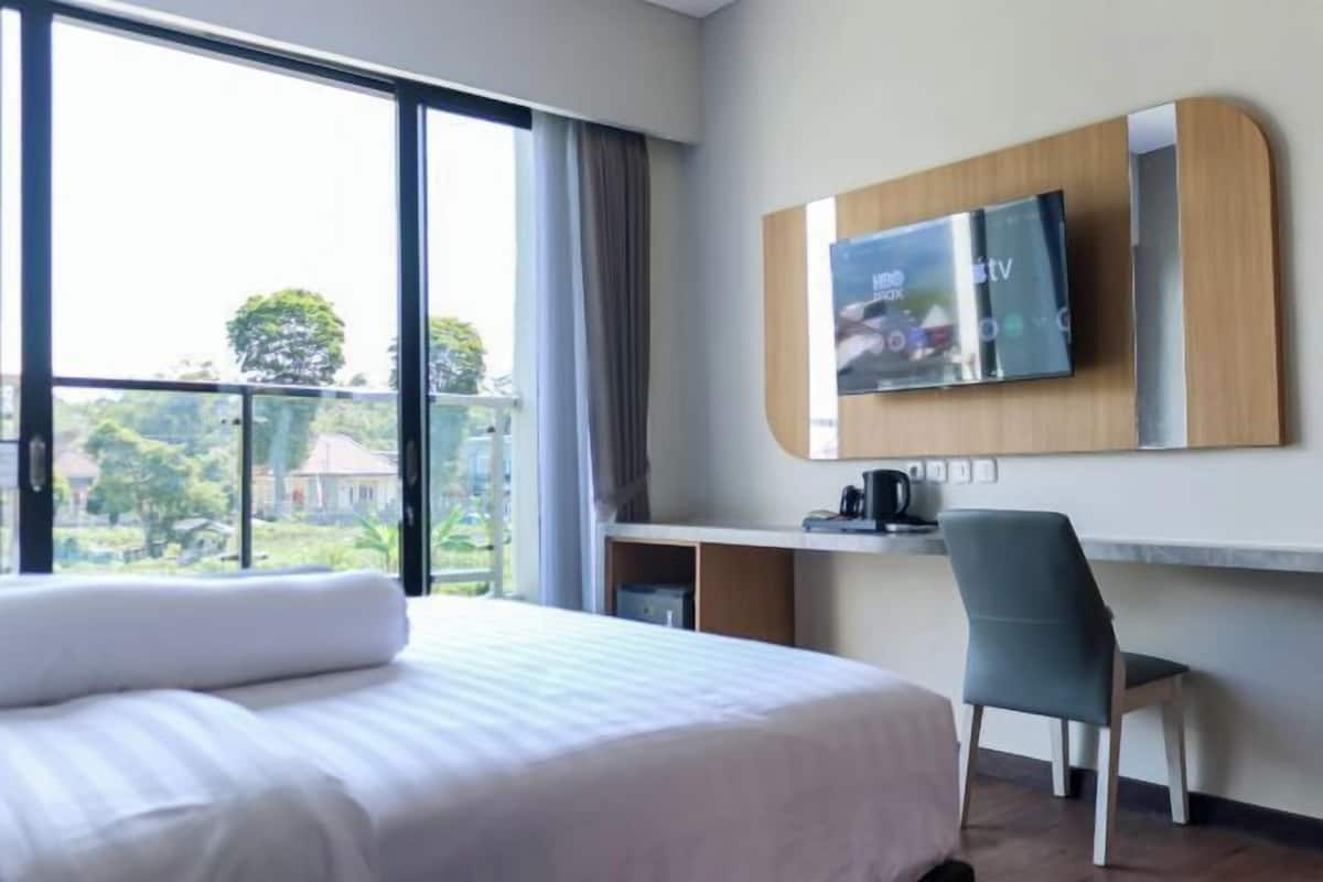 Habitación de hotel con cama, escritorio con televisor, una silla y vistas a zonas verdes.
