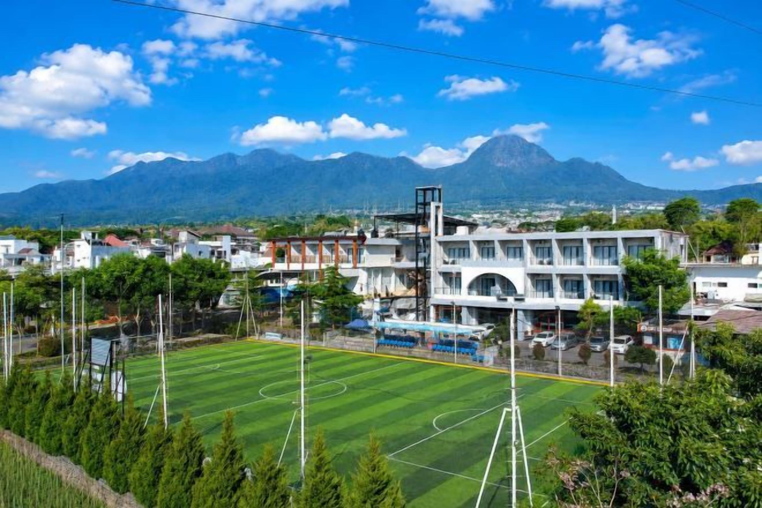 A sports field with goalposts, a building with multiple floors, and a mountain in the background.