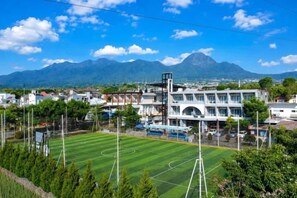 A sports field with goalposts, a building with multiple floors, and a mountain in the background. - Azana BeSt Hotel Batu (Junrejo)