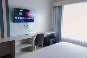 A hotel room with a bed, a desk, a chair, a TV mounted on the wall, and a window with curtains. - Azana BeSt Hotel Batu (Junrejo)